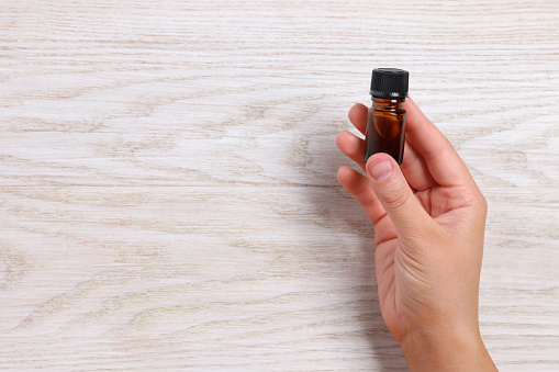 Woman with bottle of essential oil on wooden background, closeup. Space for text