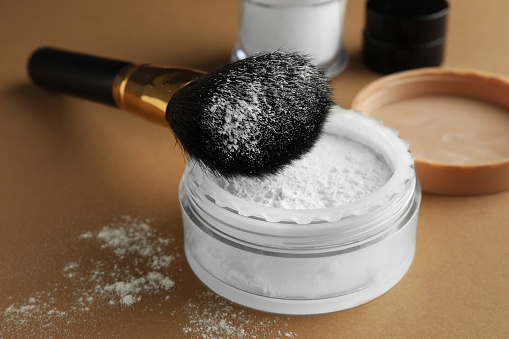 Makeup brush with rice loose face powder on brown background, closeup