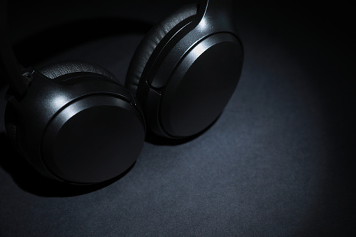 Modern wireless headphones on dark background, space for text