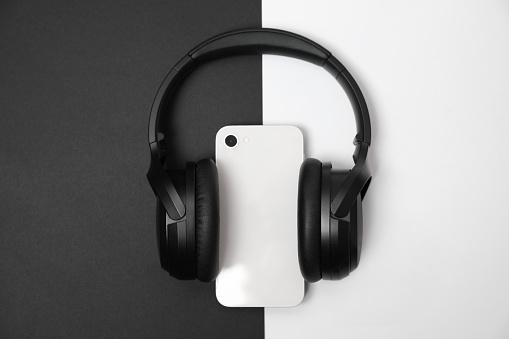 Modern wireless headphones and smartphone on color background, top view