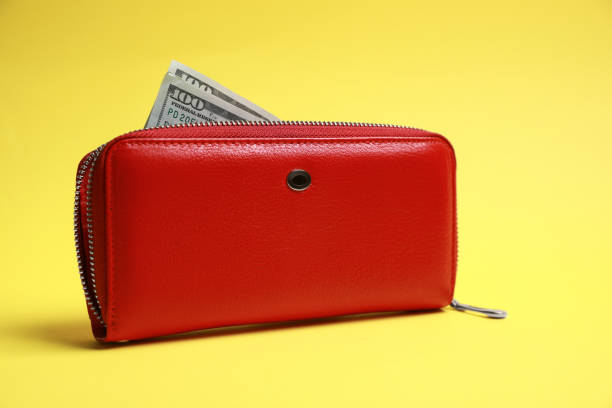 Stylish red leather purse with dollar banknotes on yellow background