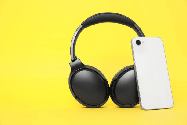 istock Modern wireless headphones and smartphone on yellow background 1918038128