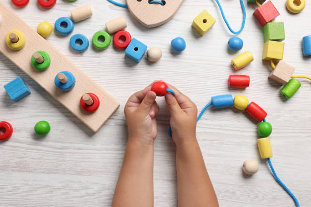 istock Motor skills development. Little child playing with wooden pieces and string for threading activity at white table, top view 1918052192