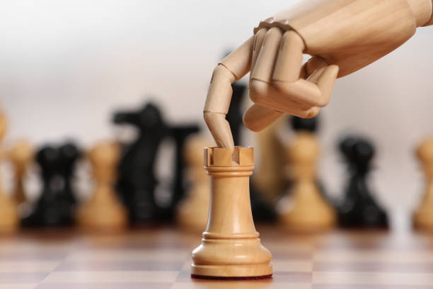 Robot moving chess piece on board against light background, closeup. Wooden hand representing artificial intelligence
