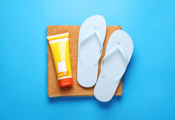 istock Flip flops, sunscreen and soft towel on light blue background, top view 1918075603