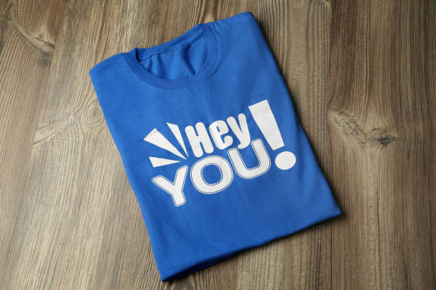 Light blue shirt with printed words Hey You on wooden table, top view