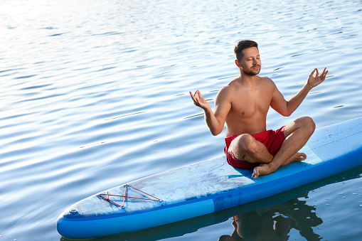 Man meditating on light blue SUP board on river
