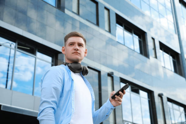 istock Man with headphones and smartphone near building outdoors, low angle view. Space for text 1918157470