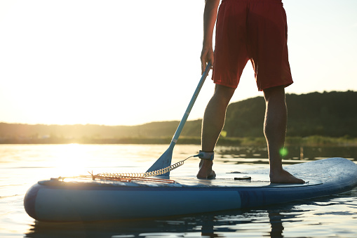 Man paddle boarding on SUP board in river at sunset, closeup