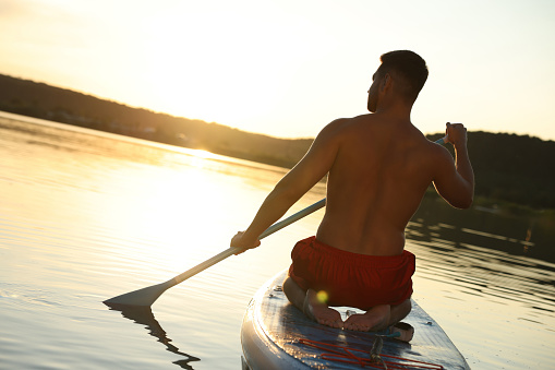 Man paddle boarding on SUP board in river at sunset, back view