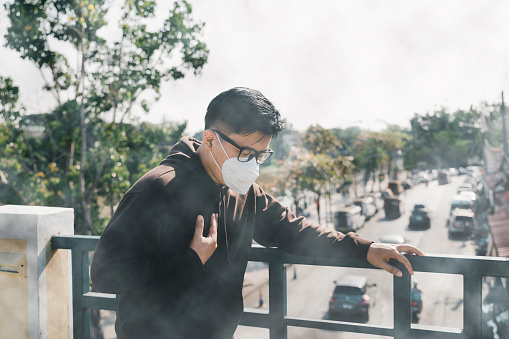 Portrait Asian man wearing an N95 mask and coughing in bad weather. Young man wearing protection mask over smog city.PM2.5 unhealthy air pollution dust smoke in the urban city, PM 2.5.health care,