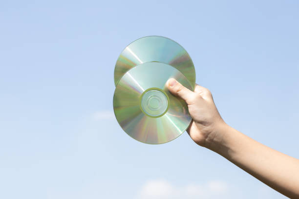 Recyclable CD disk or electric waste held in hand up on sky background. Hand holding electronic trash for recycle reduce and reuse concept to promote clean environment with recycling management. Gyre
