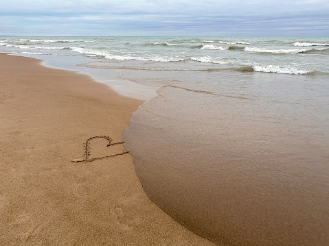 Heart on beach being washed away by wave