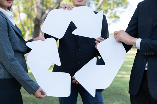 Business people holding pieces of reverse arrow icon into recycle symbol together in outdoor nature, promoting Earth cleaning day with zero waste pollution by embrace recycle reduce reuse idea. Gyre