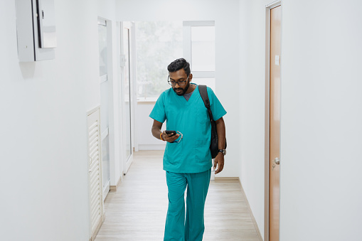 Indian healthcare worker using smartphone and leaving his work place after working hour