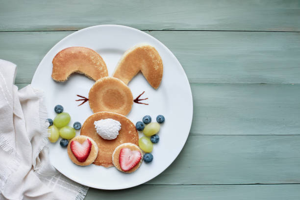 Backside of Pancake bunny for children with fruit Fun, creative pancake bunny rabbit with fluffy tail hopping away for children with whipped cream and strawberries with green grapes and blueberries as Easter eggs to encourage kids to eat healthy food bunny pancake stock pictures, royalty-free photos & images