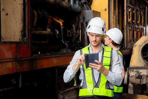 Young caucasian engineer man and woman checking train with tablet in station, team engineer inspect system transport, technician examining infrastructure, transportation and industry.