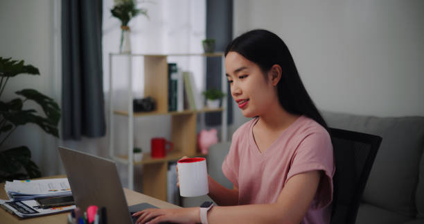 istock Young woman holding coffee to drinking while working on laptop at home. 1918671059