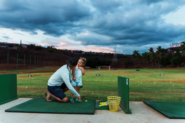 young girl practices her golf swing on driving range, view from behind