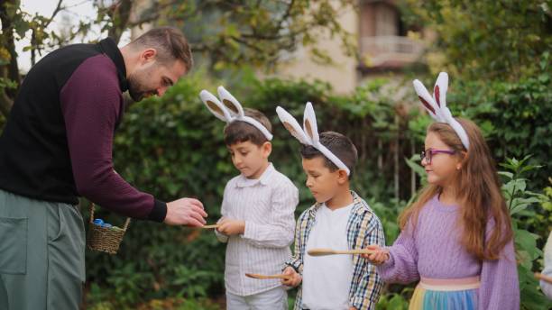 young man explaining egg and spoon race to group of children outdoors - picnic basket christianity holiday easter - fotografias e filmes do acervo