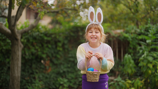 A portrait of a small cute girl on Easter egg hunt game in a back yard garden.