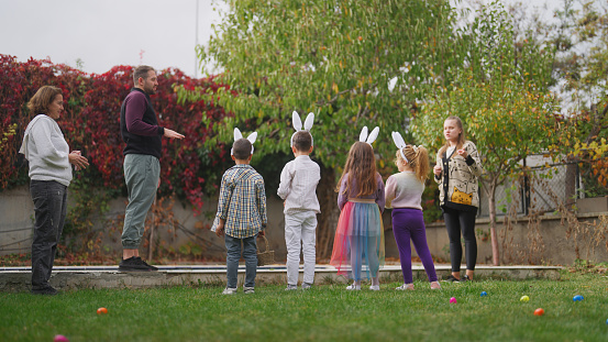 A group of excited children are running around in garden on Easter egg hunt game.