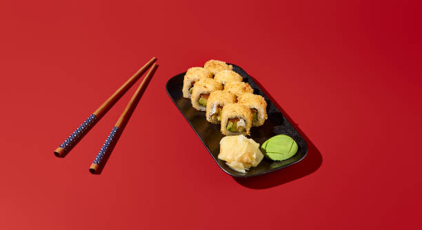 istock Tempting tempura sushi roll with salmon and avocado, presented on a black plate with chopsticks against a deep red backdrop. Perfect for an Asian restaurant ad 1918827324