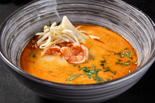 A side view of Tom Yum soup with seafood, served with lime and chili peppers, beautifully presented on a black background.