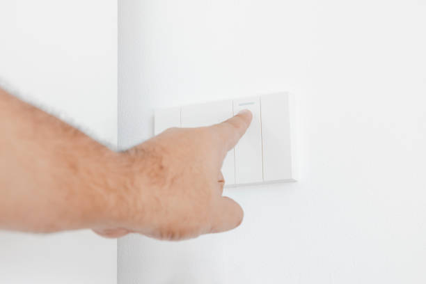 istock Man uses his finger to turn on a light switch on white wall. Plug studio apartment power supply. Light switch. Power outlet. Concept of technology, connection, power saving, energy saving. 1918833227