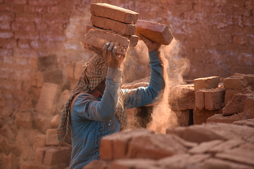 At a brick kiln in Bhaktapur, Nepal, a migrant laborer from Bihar, India, balances bricks on their head. During the winter season, seasonal laborers from various parts of Nepal and India arrive to work at the kilns.