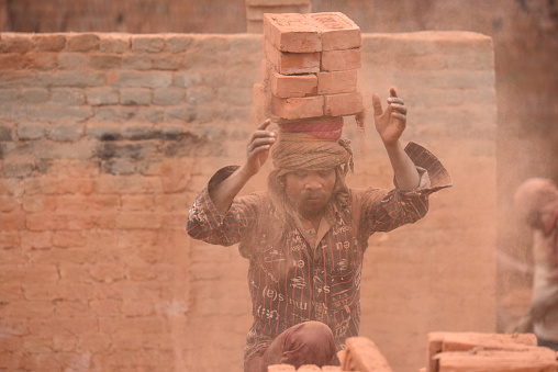 At a brick kiln in Bhaktapur, Nepal, a migrant laborer from Bihar, India, balances bricks on their head. During the winter season, seasonal laborers from various parts of Nepal and India arrive to work at the kilns.