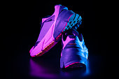 A pair of modern running shoes isolated on black background, neon coloured lighting