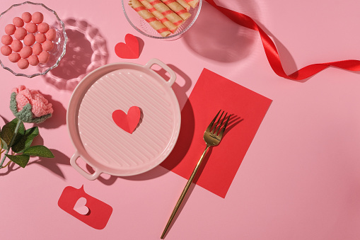 Romantic Valentine's day background and love concept with cute props decorated on a pink background. Sweet candy and chocolates, red ribbon, pan and pork are displayed. Copy space