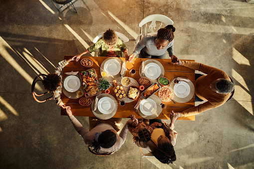 Above view of religious African American extended family holding hands while praying before lunch at dining table. Copy space.