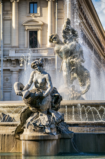 A detail of the beautiful Fountain of the Naiads in Piazza della Repubblica, in the heart of Rome, on the edge of the Rione Monti. The Fountain of the Naiads was built in 1870 during the pontificate of Pope Pius IX, a few days before the conquest of Rome by the troops of the Kingdom of Italy and the end of the temporal power of the papacy, by the artists Mario Rutelli e Alessandro Guerrieri. In the photo: In the foreground the figure of a Nymph, while behind the figure of Glaucus grabbing a dolphin, symbol of man's primacy over nature. The Monti district is a popular and multi-ethnic quarter much loved by the younger generations and tourists for the presence of trendy pubs, fashion shops and restaurants, where you can find the true soul of the Eternal City. The Rione Monti, located between Via Nazionale and the Fori Imperiali, is also rich in numerous churches in Baroque style and archaeological remains. In 1980 the historic center of Rome was declared a World Heritage Site by Unesco. Image in high definition quality.