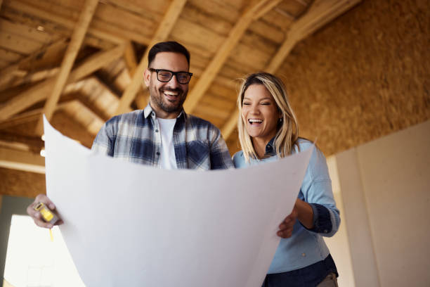 istock Below view of happy couple reading housing plans at construction site. 1918964512