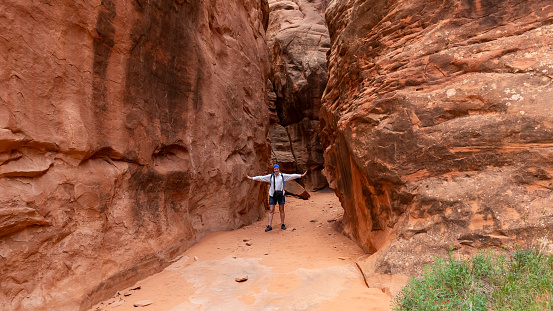 Female Traveler Hiking through Narrow Sandstone Desert Rock Canyon Trail in Fiery Furnace, Arches National Park, Utah, United States