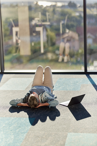 Tired female entrepreneur relaxing on floor by the computer at casual office. Copy space.