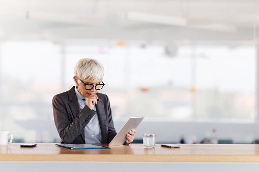 Senior businesswoman brainstorming while working on touchpad in the office. Copy space.