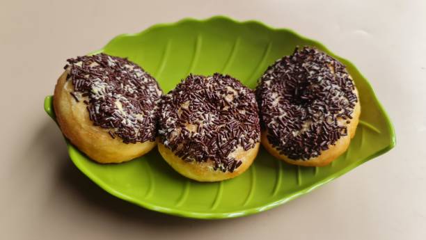 istock Three donut cakes with chocolate sprinkles, served on a green leaf-shaped plate, isolated in beige background. 1919057728