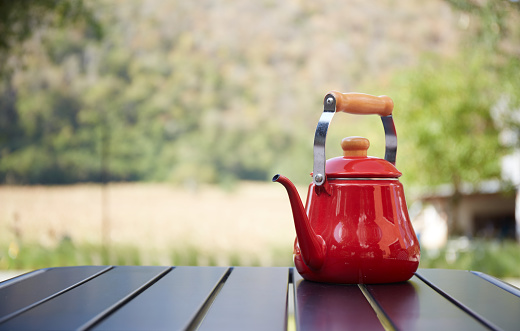Red teapot on a wooden table in a garden background