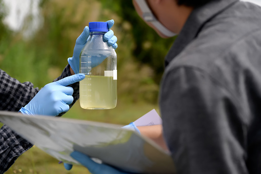 Environmental Engineers Inspect Water Quality with Note and Collect water samples in The Field Near Farmland, Fish Ponds, Natural Water Sources that may be Contaminated by Suspicious Pollution Sites.