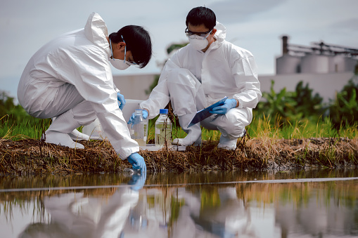 Factory scientists or biologists wear protective clothing while Collecting water samples in natural water sources near farmland. Concept of Chemical protection may leak into natural water sources.