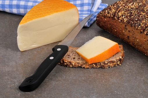 Piece of Saint-Paulin cheese on a slice of seeded bread with a knife close-up