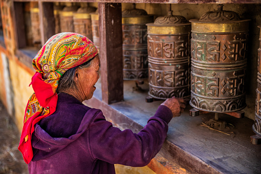Old Tibetan woman turning the prayer wheels in a small village, Upper Mustang. Mustang region is the former Kingdom of Lo and now part of Nepal,  in the north-central part of that country, bordering the People's Republic of China on the Tibetan plateau between the Nepalese provinces of Dolpo and Manang.