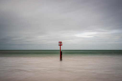 A single post (groyne) in the sea, in Swanage beach, Dorset. the waves are lapping past the post. The day is overcast and cloudy