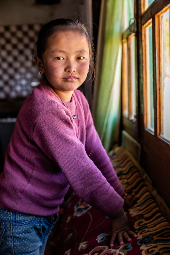 Tibetan  little girl looking through the window, Lo Manthang, Upper Mustang. Mustang region is the former Kingdom of Lo and now part of Nepal,  in the north-central part of that country, bordering the People's Republic of China on the Tibetan plateau between the Nepalese provinces of Dolpo and Manang.