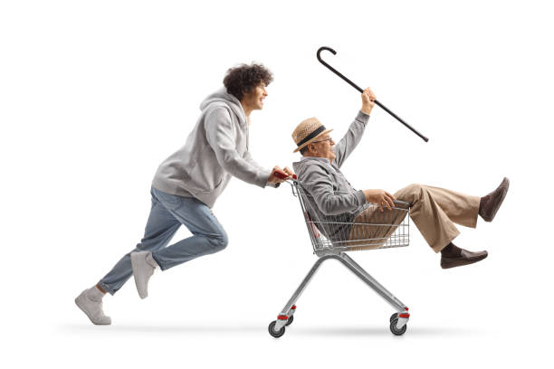 istock Guy running and pushing a senior man with a cane inside a shopping cart 1919181748