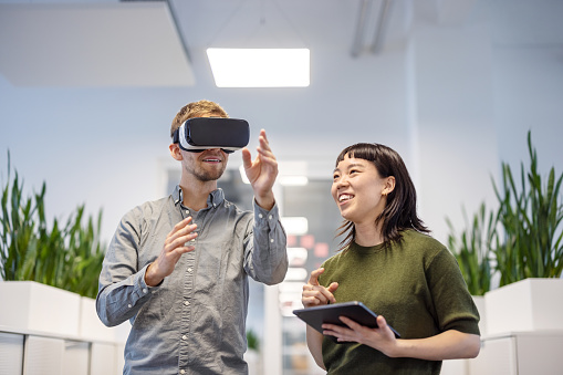 Young man using VR glasses with female colleague holding digital tablet at office. Business professionals testing the new virtual reality software in office.