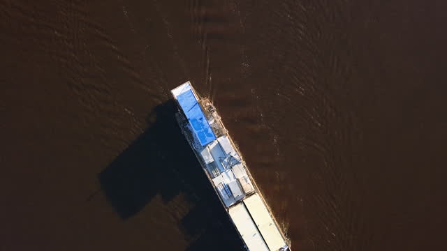 Aerial top view of a ship sailing on the brown river. Clip. Concept of water transport and travelling